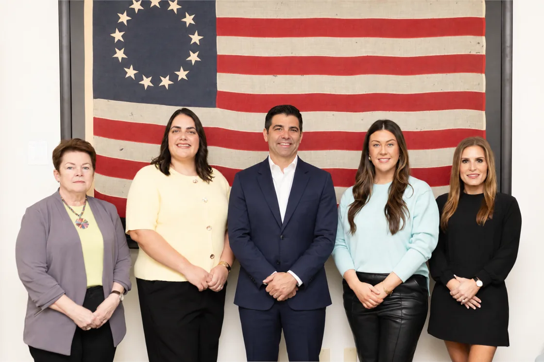 Five members of the Highflyer team standing together in front of a framed antique American flag